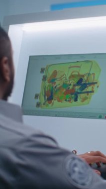 Afrikalı Amerikalı Güvenlik Subayı Modern Yazılım kullanarak Bilgisayar Monitörlerinde Bavul Gösterimini Denetliyor. Uçak Uçuşu için havaalanı güvenlik kontrol noktasındaki konveyör bandında gelişmiş X-ray taraması. Arka Görünüm