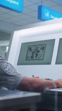 Havaalanı Güvenlik Kontrol Noktası: Afrikalı Amerikan Güvenlik Subayı Bilgisayar Ekranlarında bagaj taramasını izliyor. Röntgen tarama teknolojisi konveyör bandında. Dolly Shot. Dikey Çekim.