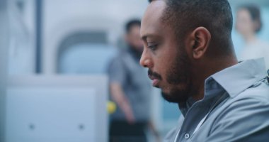 Havaalanı Güvenlik Kontrol Noktası: Afrikalı Amerikalı Güvenlik Subayı Yolcu Gösterimini İzliyor. Metal dedektöründen geçen kadına odaklanın. Uçağa biniş için Kapılar Tarayıcı.