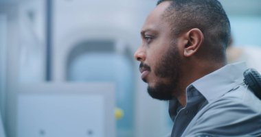 Havaalanı Güvenlik Kontrol Noktası: Afrikalı Amerikalı Güvenlik Subayı Yolcu Gösterimini İzliyor. Metal dedektöründen geçen kadına odaklanın. Uçağa biniş için Kapılar Tarayıcı.