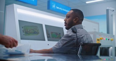 Afrikalı Amerikalı Güvenlik Subayı Modern Yazılım kullanarak Bilgisayar Monitörlerini Tarıyor. Ön planda, Yolcular Uçak Uçuşunun İncelemesi İçin Kişisel Ait Koyuyor.