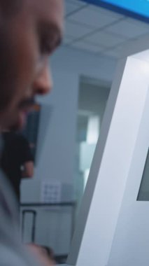 Havaalanı Güvenlik Kontrol Noktası: Afro-Amerikan Güvenlik Görevlisi Ekranda X-ray bagaj taramasını izliyor, Valiz Kullanıcı Yazılımında Şüpheli Nesne Buluyor, Telsiz-Talkie ile Konuşuyor. Dikey Çekim.