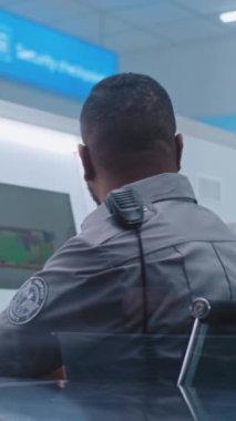 Afrikalı Amerikalı Güvenlik Subayı Modern Yazılım kullanarak Bilgisayar Monitörlerini Tarıyor. Ön planda, Yolcular Uçak Uçuşunun İncelemesi İçin Kişisel Ait Koyuyor.