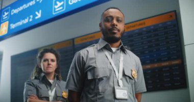 Uluslararası Havalimanı Terminalindeki Profesyonel TSA çalışanlarının Portresi: Kameraya Bakan Üniformalı İki Güvenlik Memuru. Arka planda Dijital Uçuş Bilgileri Ekranı. Doli Vuruşu.