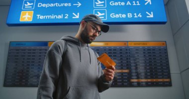 Havaalanı Terminali: Sırt çantalı adam akıllı telefon kullanarak uçuş bilgileri tarama bileti kontrol ediyor. Gezgin Tatile Çıkıyor. Arka plandaki Yolcular için Çeşitli İnsanlar ve Dijital Ayrılış Kurulu.