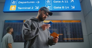 Havaalanı Terminali: Sırt çantalı adam akıllı telefon kullanarak uçuş bilgileri tarama bileti kontrol ediyor. Gezgin Tatile Çıkıyor. Arka plandaki Yolcular için Çeşitli İnsanlar ve Dijital Ayrılış Kurulu.