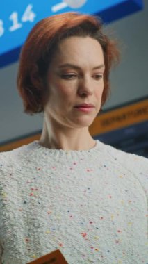 Havaalanı Terminali: Uçuş bilgilerini kontrol etmek için akıllı telefonu kullanan kadın uçak bileti. Arkaplanda Dijital Geliş ve Gidiş Bilgileri Görüntüsü. Seyahate çıkan bir turist. Dikey Çekim.