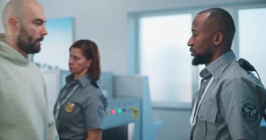 Havaalanı Terminali 'ndeki Güvenlik Kontrol Noktası: Afrikalı Amerikalı Güvenlik Subayı Yetişkin Adam' ı Uçağa binen şüpheli nesneler için kontrol ediyor. TSA tarama prosedürleri. Gezgin Tatile Çıkıyor.