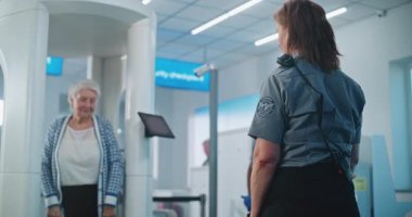 Havaalanı Terminali 'ndeki güvenlik kontrol noktası: Kadın güvenlik görevlisi, Metal Detektörü Kapıları Taradıktan sonra Uçak Uçuşu için Yaşlı Kadın Denetliyor. TSA tarama prosedürleri. Gezgin Tatile Çıkıyor.