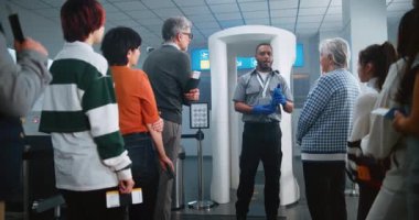 Havalimanı Güvenlik Kontrol Noktası: Afro-Amerikan Güvenlik Subayı, çeşitli kişilere, yolculara, TSA Uçuş Tarama Prosedürleri ile ilgili talimatlar verdi. Seyahate çıkan turist kuyruğu.