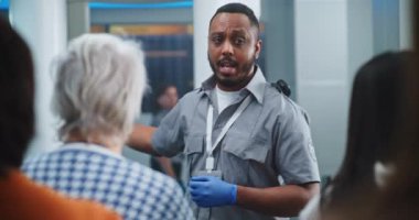 Havaalanı Terminali Güvenlik Kontrol Noktası: Afro-Amerikan Güvenlik Subayı Çeşitli Kişilere, Yolculara Metal Detektör Tarayıcı Kapıları Hakkında Bilgi Veriyor. Gezginler Kuyruğu Tarama İşlemlerini Bekliyor.