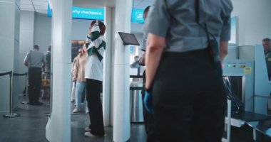 Havaalanı Terminali: Metal dedektöründen geçen çeşitli insanlar. Afro-Amerikan Güvenlik Subayı yolcuları Tablet Bilgisayar 'dan uçağa binmek için kontrol ediyor. Gezginler Tatile Çıkıyor.