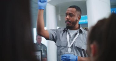 Havaalanı Güvenlik Kontrol Noktası: Afro-Amerikan Ulaşım Güvenliği Memuru Çeşitli Kişilere, Yolculara Metal Detektör Tarayıcı Kapıları, Tarama Prosedürleri hakkında bilgi veriyor. Gezginlerin Kuyruğu Gezintiye Çıkıyor.