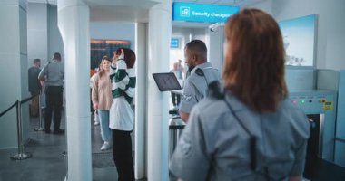 Havaalanındaki Ulaşım Güvenlik Hattı Metal Detektör Kapıları 'ndan geçen çeşitli insanlar. Afro-Amerikan Güvenlik Subayı Yolcuları Uçuş için kontrol ediyor, Tablet Bilgisayar kullanıyor.