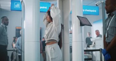 Havaalanı terminalindeki güvenlik kontrolüne göre Asyalı kadın Tarama Kapısı 'ndan geçiyor. Bayan Güvenlik Görevlisi, Yolcu 'yu kontrol ediyor. Uçağa biniş, Cep Telefonu Bulma. TSA Tarama Prosedürleri.