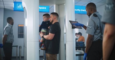 Havaalanı güvenlik kontrol noktası: Metal dedektör kapısından geçen çocuklu aile. Yolcu tarama prosedürünü kontrol eden güvenlik görevlileri, Tablet Bilgisayar kullanarak uçağa biniyorlar..
