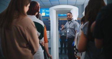 Havaalanı Güvenlik Kontrol Noktası: Afro-Amerikan Güvenlik Görevlisi Çeşitli Kişilere, Metal Detektör Tarayıcı Kapıları Yolcularına TSA Tarama Prosedürleri hakkında bilgi veriyor. Gezginlerin Kuyruğu Gezintiye Çıkıyor.