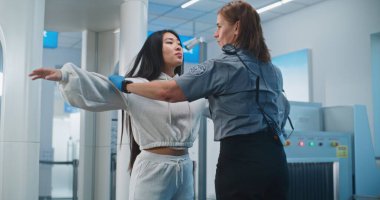 Havaalanı Terminali 'ndeki güvenlik kontrol noktası: Kadın güvenlik görevlisi, metal dedektörü Gates' i taradıktan sonra Asyalı kadını kontrol ediyor. Uçağa binmek için Ulaşım Güvenliği İdaresi İnceleme Prosedürleri. Turist Tatile Çıkıyor.