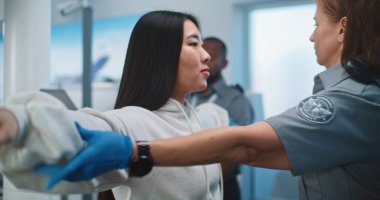 Havaalanı Terminali 'ndeki Güvenlik Kontrol Noktası: Kadın Güvenlik Subayı, Asyalı Kadın Bedenini Uçak Uçuşu için Şüpheli Eşyalar İçin Denetliyor. TSA tarama prosedürleri. Turist Tatile Çıkıyor.