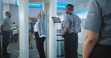 Havaalanı Terminali: Metal dedektör kapısından geçen yaşlı kadın. Güvenlik Subayı, Yolcuyu Tablet Bilgisayar 'da yolcu uçağına binmek için kontrol ediyor. Gezginlerin Kuyruğu Ekranı Bekliyor.