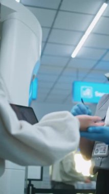 Havaalanı Güvenliği Kontrol Noktası: TSA 'da el temizliği yapan kadın güvenlik görevlisi, uçağa binmek için fırçayla Asyalı kadını tarıyor. Patlayıcı madde izlerini tespit etmek için ETD Yöntemi. Dikey Çekim.