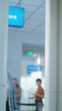 Havaalanındaki TSA Güvenlik Kontrol Noktası: Metal dedektöründen geçen yaşlı kadın. Güvenlik Subayı, Yolcu Tarayıcı Uçuş prosedürünü kontrol ediyor, Tablet Bilgisayar kullanıyor. Dikey Çekim.