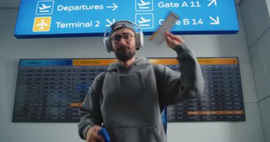 Uluslararası Havalimanı Terminali: Mutlu Adam Dansının Portresi, Uçak Bileti Tutma, Kamera Bakışı. Arkaplanda Geliş ve Gidiş Bilgileri Görünümü. Turist Tatile Çıkıyor.