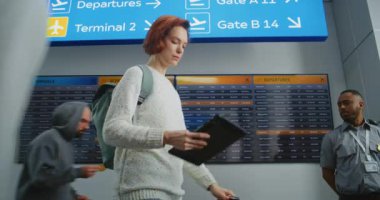 Havaalanı Terminali: Dijital Tablet Bilgisayar kullanan kadın, Geliş ve Gidiş Bilgileri Ekranında Uçuş Aranıyor. Turist Tatile Gidiyor. Arkaplanda Bir İnsan Kalabalığı.