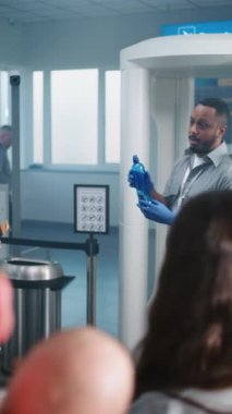 Havaalanı Güvenlik Kontrol Noktası: Afro-Amerikan Güvenlik Subayı TSA Tarama Yöntemlerini Çeşitli Kişilere, Yolculara Açıkladı. Tatil gezilerine çıkan gezginler kuyruğu. Dikey Çekim.