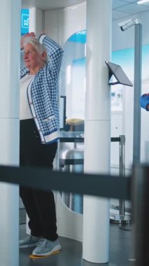 Havaalanı TSA Güvenlik Hattı: Yaşlı Kadın ve Adam Metal Detektör Tarayıcısından Geçiyor. Afro-Amerikan Güvenlik Subayı Yolcu Tarama Prosedürünü kontrol ediyor, Tablet Bilgisayar kullanıyor. Dikey Çekim.