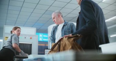 Havaalanındaki Güvenlik Kontrol Noktası: Bayan TSA çalışanı, X-ray taraması için yolcuların kişisel eşyalarını ve çantalarını aldı. Tarama işlemi sırasında çeşitli insanlar, gezginler. Arkaplanda Metal Detektör Kapıları.