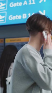 Kalabalık Havaalanı Terminali: Cep telefonuyla konuşan genç adam, uçağa binmeyi bekliyor. Seyahate çıkan bir turist. Arka planda, Geliş ve Gidiş Görünümü, Farklı İnsanlar Yürüyor. Dikey Çekim