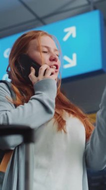 Kalabalık Havaalanı Terminali: Kafkas Kadın Tutucu Uçak Bileti, Cep Telefonu ile Konuşma, Uçuş Bilgilerini Denetleme. Dijital Geliş ve Gidiş Görünümü, Farklı İnsanlar Yürüyüşü. Dikey Çekim.