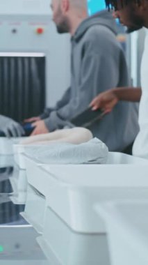 Havaalanı Güvenlik Kontrol Noktası: Çeşitli İnsanlar Metal Detektör X-ray Taraması için Kişisel Eşyalar Koyuyor. Havaalanı personeli, Afro-Amerikan Güvenlik Subayı TSA tarama prosedürünü kontrol ediyor. Dikey Çekim.