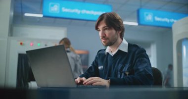 Havaalanı Güvenlik Kontrol Noktası: TSA İşçisinin Laptop kullanarak, Kameraya bakarak portresi. Seyahat Güvenliği Ulaştırma Güvenlik İdaresi. Arka planda, Havalimanı Personel İdaresi Taraması