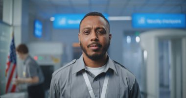 Havaalanı Güvenlik Kontrol Noktası: Kameraya bakan üniformalı Afro-Amerikan TSA memurunun portresi. Seyahat Güvenliği Ulaştırma Güvenlik İdaresi. Arka planda, havaalanı personeli çalışıyor.