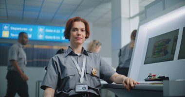Havaalanı Güvenlik Kontrol Noktası: Kameraya bakarak gülümseyen kadın güvenlik görevlisinin portresi. Bilgisayar ekranları bagaj tarama prosedürünün X-ray görüntülerini gösteriyor. Arka planda, havalimanı personeli çalışıyor.