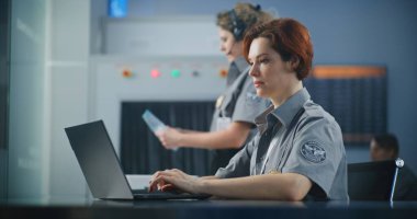 Havaalanı Güvenlik Kontrol Noktası: Dizüstü bilgisayarda çalışan kadın güvenlik subayı. Seyahat Güvenliği Ulaştırma Güvenlik İdaresi. Arka planda, havalimanı personeli tarama prosedürleri.