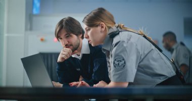 Havaalanı Güvenlik Kontrol Noktası: Laptop kullanan iki farklı havaalanı işçisi, güvenlik konularını tartışıyor. Seyahat Güvenliği Ulaştırma Güvenlik İdaresi. Arka planda, havaalanı personeli çalışıyor.