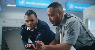 Havaalanı Güvenlik Kontrol Noktası: Afro-Amerikan Ulaşım Güvenliği İşçileri Laptop kullanıyor, Güvenlik konularını tartışıyor. Seyahat Güvenliği Ulaştırma Güvenlik İdaresi. Arka planda, havaalanı personeli çalışıyor.