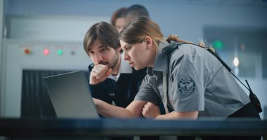 Havaalanı Güvenlik Kontrol Noktası: Laptop kullanan iki farklı havaalanı işçisi, güvenlik konularını tartışıyor. Seyahat Güvenliği Ulaştırma Güvenlik İdaresi. Arka planda, havaalanı personeli çalışıyor.