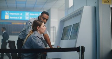 Havaalanı Güvenlik Kontrol Noktası: Modern Yazılım Kullanılarak Bilgisayar Ekranlarında Bagaj Tarama İşlemlerinin X-ray görüntülerini izleyen iki çok ırklı güvenlik görevlisi. Bagaj Kısıtlamalarına Odaklan İmzalayın