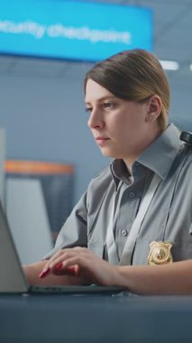 Havaalanı güvenliği: kadın havaalanı görevlisi Laptop kullanıyor, gülümsüyor ve kameraya bakıyor. Ulaşım Güvenlik İdaresi. Arka planda, havalimanı personeli tarama prosedürleri. Dikey Çekim.