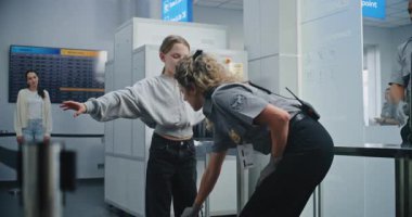 Havaalanı Terminalindeki güvenlik kontrol noktası, havaalanı personeli TSA taraması. Metal dedektörlü genç kızı muayene eden bayan memur, yolcu uçuşu için bavullu genç yolcuyu gezdiriyor..