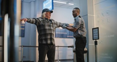 Güvenlik Kontrol Noktası: Afrikalı Amerikalı Ulaşım Güvenliği Memuru Havaalanı Terminalinde Yaşlı Adamı Kontrol Ediyor. Uçağa binmek için yolcu tarama prosedürleri ve güvenlik kontrolü. Kıdemli Gezgin Seyahate çıkıyor.