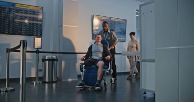 Havaalanı terminalindeki güvenlik kontrol noktası: Tekerlekli sandalyeden kalkan protez bacaklı adam, X-ray metal dedektörü tarayıcısını geçiyor, güvenlik personeli yardım ediyor. Tarama İşlemleri sırasında Yolcular.