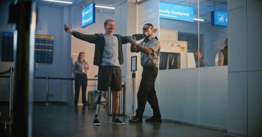 Havaalanı Terminali 'ndeki güvenlik kontrol noktası: Afro-Amerikan Güvenlik Subayı, Biniş Uçuşu için Protez Ayaklı Genç Adamı Denetliyor. TSA tarama prosedürleri. Engelli turist. Tam Vuruş.