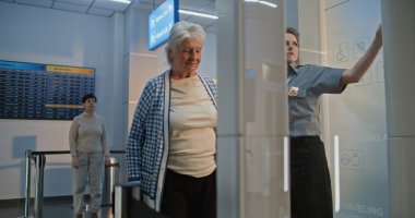 Havaalanı Terminali 'ndeki güvenlik kontrol noktası: Tekerlekli sandalyeden kalkan yaşlı kadın, metal detektör tarama kapısından geçen güvenlik görevlisi ona yardım ediyor. Tarama sırasında kıdemli turist.