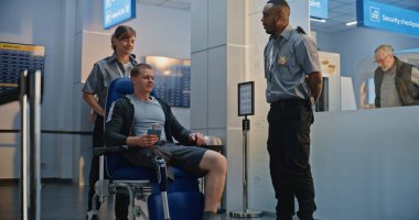 Güvenlik Kontrol Noktası: Afro-Amerikan Ulaşım Güvenliği Memuru Adamı Havalimanı Terminali 'ndeki tekerlekli sandalyede biyonik protez bacakla kontrol ediyor. Uçağa binmek için yolcu tarama prosedürü. Engelli Yolcu