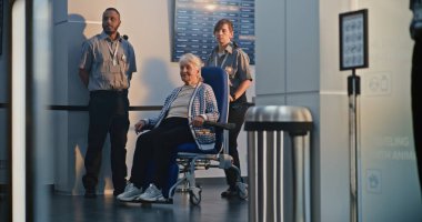 Havaalanı Terminali 'ndeki güvenlik kontrol noktası: Yaşlı kadının tekerlekli sandalyeden kalkmasını denetleyen kadın güvenlik görevlisi. Uçağa binmek için Ulaşım Güvenliği İdaresi İnceleme Prosedürleri. Kıdemli Turist Seyahate Çıkıyor.